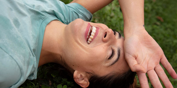 Una mujer sonríe acostada en la grama, y con mucho calor